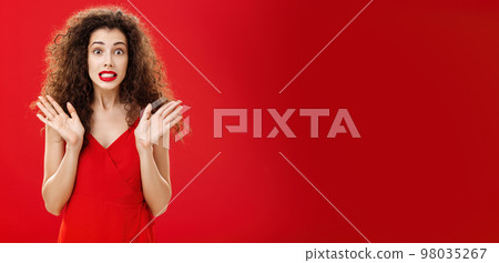 Woman feeling nervous and concerned messing up important papers clenching teeth and popping eyes being worried and troubled waving raised palms in clueless and perplexed gesture over red background 98035267