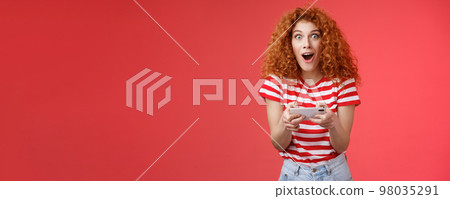 Impressed excited good-looking redhead curly woman hold smartphone horizontal open mouth fascinated stare camera thrilled astonished win passed level game happy playing cool app red background Impressed excited good-looking redhead curly woman hold smartphone horizontal open mouth fascinated stare camera thrilled astonished win passed level game happy playing cool app red background 98035291
