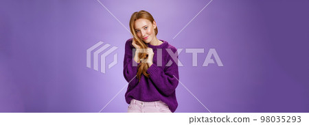 Attractive feminine and shy redhead girl flirting looking cute and tender at camera playing with comb of hair looking at camera coquettish and silly posing against purple background Attractive feminine and shy redhead girl flirting looking cute and tender at camera playing with comb of hair looking at camera coquettish and silly posing against purple background 98035293