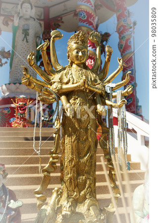 Beautiful Golden Thousand-hand Guan Yin statue stands in front of the pavilion. 98035809