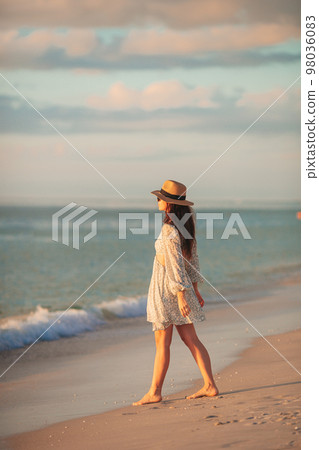 Young beautiful woman at straw hat on the beach at sunset Young beautiful woman at straw hat on the beach at sunset 98036083