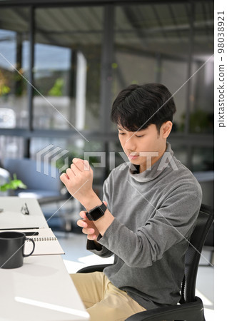 Handsome young Asian male developer or business office worker wearing his smartwatch 98038921