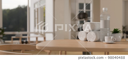 Fitness lounge, towels, a bottle of water, a coffee cup on wood table over blurred background 98040488