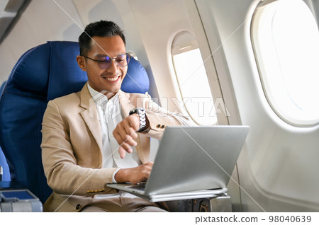 Successful Asian businessman checking his watch for the arrival time, on the flight for business trip. Successful Asian businessman checking his watch for the arrival time, on the flight for business trip. 98040639