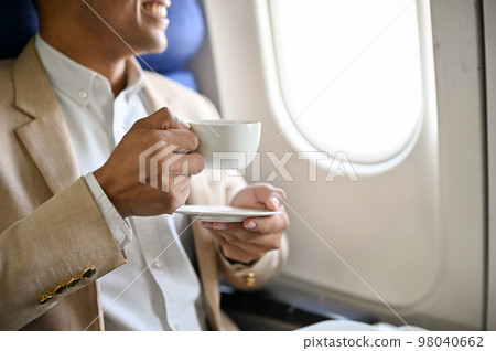 Successful Asian businessman holds a cup of coffee and sip coffee during the flight for business trip Successful Asian businessman holds a cup of coffee and sip coffee during the flight for business trip 98040662