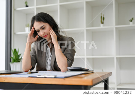 Stressed and unhappy Asian businesswoman sits at her desk suffering from headache Stressed and unhappy Asian businesswoman sits at her desk suffering from headache 98041222