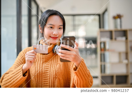 A pretty Asian female holding a smartphone and a credit card, using an online mobile banking A pretty Asian female holding a smartphone and a credit card, using an online mobile banking 98041237