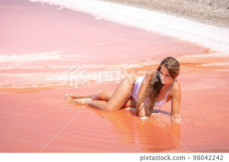 Young woman with long hair in pink salty lake with crystals of salt. Extremely salty pink lake, colored by microalgae with crystalline salt depositions. Spa, beauty and health care concept. Young woman with long hair in pink salty lake with crystals of salt. Extremely salty pink lake, colored by microalgae with crystalline salt depositions. Spa, beauty and health care concept. 98042242