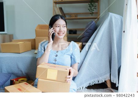 Starting small business entrepreneur of independent Asian female online seller talking on the phone with a customer and packing products for delivery to the customer. and SME delivery concept. 98042243