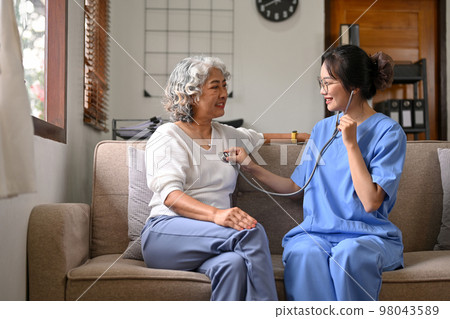 Professional Asian female doctor hold stethoscope listen to elderly female patient's heart rate 98043589