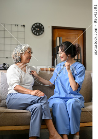 Professional Asian female doctor visiting her retire female patient at home, checking heart beat's 98043591