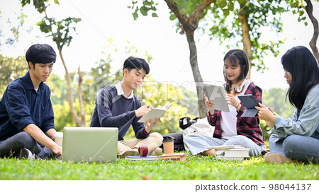 Happy Asian college students are working on their project together while relaxing in the park. Happy Asian college students are working on their project together while relaxing in the park. 98044137