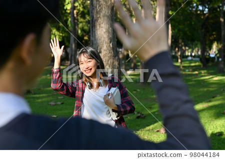 Female student greeting or saying good bye to her friend at the park, waving hand, bye bye gesture. Female student greeting or saying good bye to her friend at the park, waving hand, bye bye gesture. 98044184