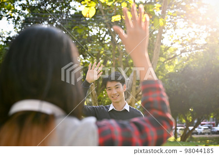 Handsome Asian male college student waving hand to his female friend Handsome Asian male college student waving hand to his female friend 98044185