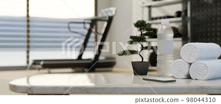 Copy space on table with bottle of water and towels over blurred background of fitness with treadmill Copy space on table with bottle of water and towels over blurred background of fitness with treadmill 98044310
