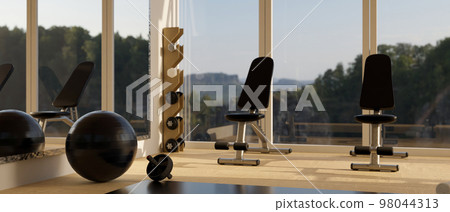 Modern fitness gym interior with sport equipments, yoga ball, dumbbells, abs wheel, and bench 98044313