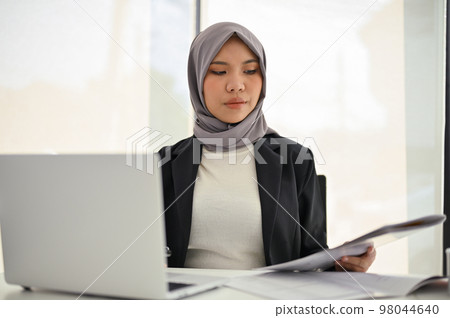 Professional Asian Muslim businesswoman reviewing the report, working in her office. Professional Asian Muslim businesswoman reviewing the report, working in her office. 98044640