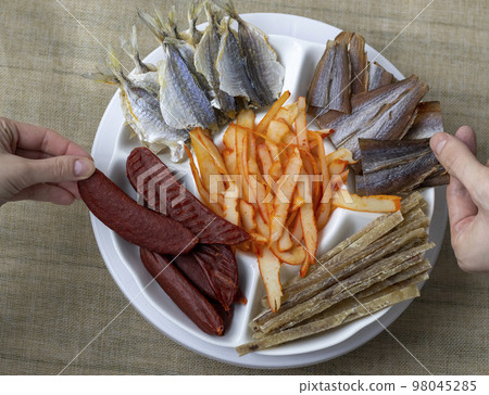 Dried Seafood Mix with Squid, Mussels, Tuna, Yellow Minke, Dried Caviar. Top View. Cured Dehydrated Fish Fillet as Beer Snack Nice Serving. In White Round Plate. Company of people take an appetizer. Dried Seafood Mix with Squid, Mussels, Tuna, Yellow Minke, Dried Caviar. Top View. Cured Dehydrated Fish Fillet as Beer Snack Nice Serving. In White Round Plate. Company of people take an appetizer. 98045285