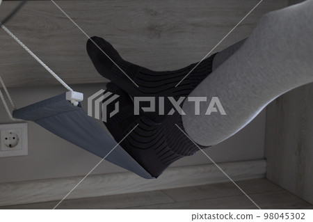 Hammock footrest under the desk. Women's feet lifted off the floor. Hammock footrest under the desk. Women's feet lifted off the floor. 98045302