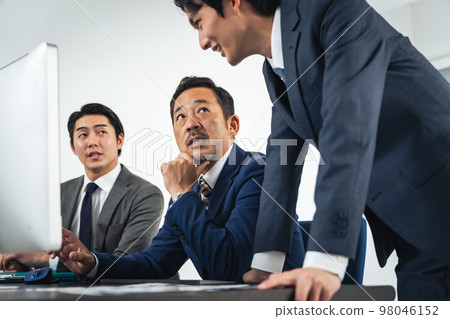Group of business people having a meeting while looking at the computer screen Group of business people having a meeting while looking at the computer screen 98046152