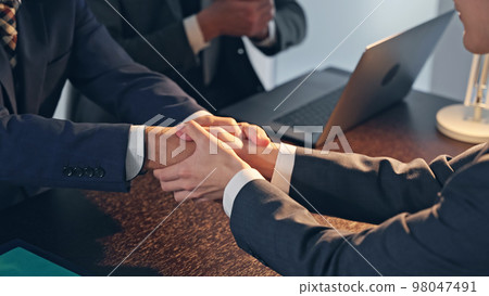 Businessmen shaking hands in a dark office 98047491