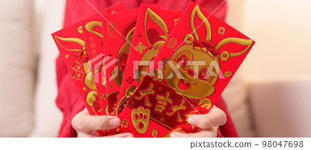 woman holding Chinese red envelope with golden rabbit and blessing word, money gift for happy Lunar New Year holiday. Chinese sentence means happiness, healthy, Lucky and Wealthy woman holding Chinese red envelope with golden rabbit and blessing word, money gift for happy Lunar New Year holiday. Chinese sentence means happiness, healthy, Lucky and Wealthy 98047698