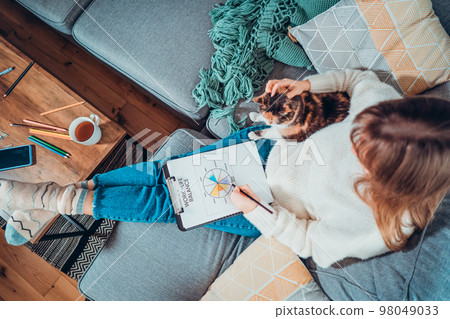 Top view relaxed young woman drawing work-life balance wheel sitting on the sofa with cat pet at home. Self-reflection and life planning. Coaching tools. Finding Balance in Your Life. Selective focus. Top view relaxed young woman drawing work-life balance wheel sitting on the sofa with cat pet at home. Self-reflection and life planning. Coaching tools. Finding Balance in Your Life. Selective focus. 98049033