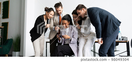 a team of colleagues in the office watches with interest how one employee plays a mobile phone a team of colleagues in the office watches with interest how one employee plays a mobile phone 98049304