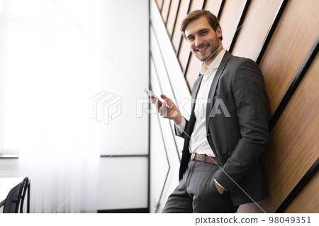 young male businessman in a business suit with a phone in his hands on the background of office 98049351