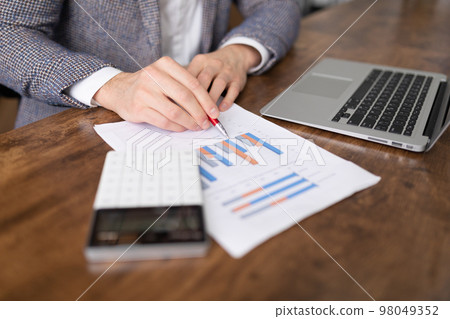 a businessman follows a sales chart in the form of columns on a table next to a laptop and a 98049352