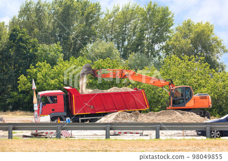Construction road equipment, excavator and truck, at the road repair construction site on a summer day. 98049855