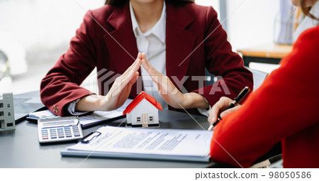 Female real estate agent is use hands to protect red roof for the concept of real estate investment about house trading, purchase at desk in office . 98050586
