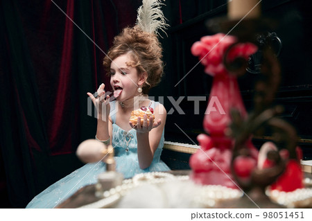Portrait of cute little girl, child in image of medieval royal person funny eating cake Portrait of cute little girl, child in image of medieval royal person funny eating cake 98051451