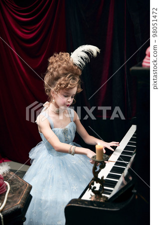 Portrait of beautiful little girl, child in image of medieval royal person in elegant dress sitting at the piano and playing Portrait of beautiful little girl, child in image of medieval royal person in elegant dress sitting at the piano and playing 98051472