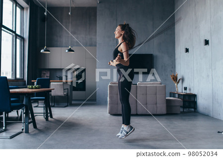 Fit woman skipping rope. Girl exercising with jumping rope at home. 98052034