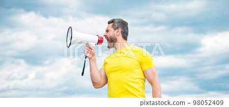man in yellow shirt yelling in loudspeaker on sky background 98052409