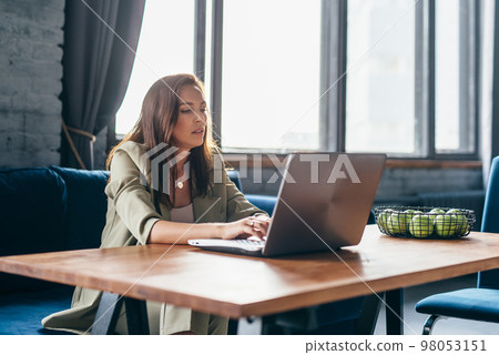 Woman at home sits at her desk and looks at her laptop screen Woman at home sits at her desk and looks at her laptop screen 98053151