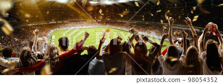 Back view of football, soccer fans cheering their team with flag and posotove emotions at crowded stadium at evening time. Concept of sport, hobby, leisure time, football 98054352