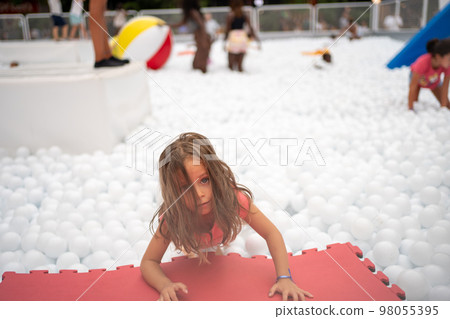 Happy little girl playing white plastic balls pool in amusement park. 98055395