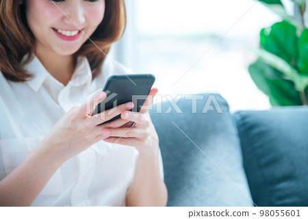 Asian woman holding smartphone with E-commerce Shopping online website Reading Online Article, Blog, vlog. Young Woman hands holding phone technology lifestyle. Happy Woman using digital smart phone 98055601