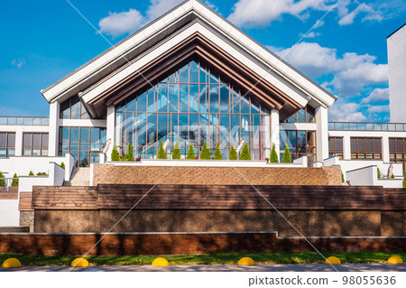 white and brown building with tall windows and green spruce around 98055636