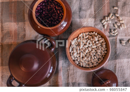 White beans in a clay deep plate on a linen tablecloth among clay pots, soft focus 98055847