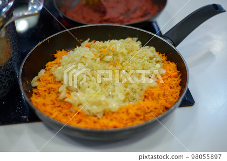 carrots and onions are fried or stewed on an electric stove in a black frying pan 98055897