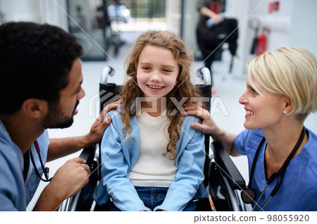 Young multiracial doctor with his colleague talking with little girl on wheelchair. 98055920