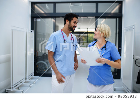 Pregnant doctor talking with her colleague at hospital corridor. Pregnant doctor talking with her colleague at hospital corridor. 98055938
