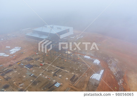 When there is heavy fog on construction site commercial buildings an tower cranes usually operate at dawn 98056065
