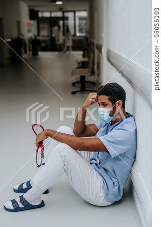 Young distressed doctor sitting at hospital corridor floor. Young distressed doctor sitting at hospital corridor floor. 98056193