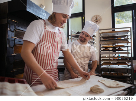 Man with down syndrom helping prepair bread in bakery with his colleague. Concept of integration people with disability into society. 98056219