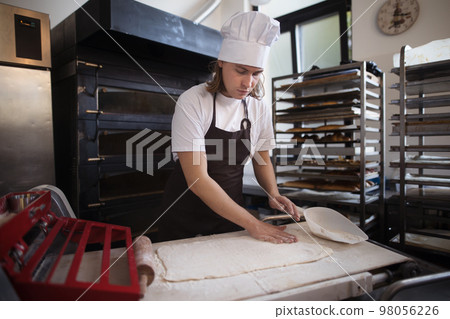 Young baker with chef cap preparing pastries in bakery. 98056226