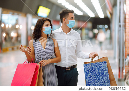 Beautiful couple in protective medical mask shopping in mall. Happy couple holding shopping bags. 98056682